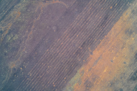 Top-down aerial photo of tilled agricultural soil with strong diagonal linear patterns. Muted cold...