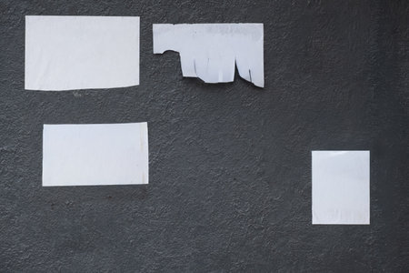 Detailed photo of a rough, dark gray wall surface featuring several blank, torn white paper remnants. Ideal grunge background or mock-up template for advertising, text, or graphic design elements.の写真素材