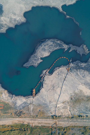 Aerial drone shot of a large industrial tailing pond (slurry storage) showing a dredge and pipeline actively moving industrial waste. Color contrast between the toxic blue water and the grey sludge.の写真素材