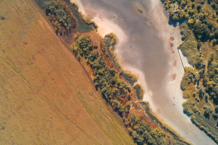 Aerial drone shot showing land use contrast between a cultivated field and a dry riverbed. The riparian zone creates a sharp ecological boundary, illustrating drought impact.の写真素材