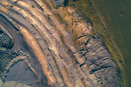 Top-down drone perspective of a massive industrial quarry. The multi-toned terraced earth highlights...
