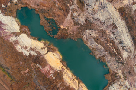 Drone shot of the vivid abstract pattern of a flooded quarry. The deep teal water sharply contrasts with the stratified layers of white and red earth, illustrating the industrial scar on the landscapeの写真素材