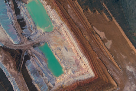 Drone shot of the vivid abstract pattern of an active mine pit. Geometric pools of bright teal chemical water contrast sharply with white rock and brown earth, illustrating severe industrial pollutionの写真素材
