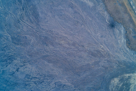 Aerial drone shot of a grey industrial slag pile slope with intricate water washout channels. Top down view of mining waste dumps in Donbas region next to a dry field edge. Abstract landscape texture and geological surface pattern.の写真素材
