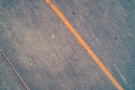 Aerial drone shot of a long straight trench cutting through a dark field. Top down view of earthworks and defensive fortifications. Landscape texture with craters. Contrast of orange clay and soil.の写真素材