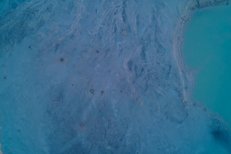 Aerial drone shot of smooth chemical sediment scarred by small crater-like vents near a cyan reservoir. Top down view of toxic industrial sludge texture and surreal lunar landscape pattern. Environmental pollution background. Minimalist.の写真素材