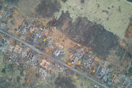 Top down view of a civilian settlement reduced to ruins and rubble concentrated along the main...