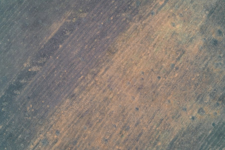 Aerial drone shot of a rough field surface featuring a mottled blend of dark grey and rust-orange soil colors. Diagonal agricultural texture and environmental background pattern in a rural landscape area.の写真素材