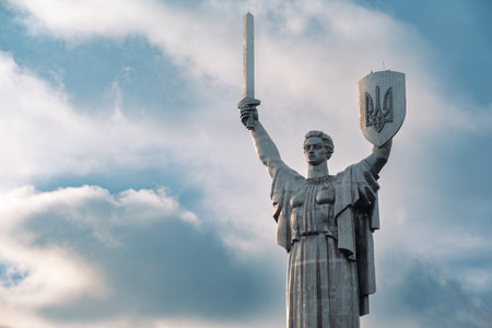 A dramatic close-up of the iconic Motherland Monument - Batkivshchyna-Maty in Kyiv, Ukraine, holding a sword and a shield with the Ukrainian coat of arms - Tryzub. The monument symbolizes national resilience and historical memory.の写真素材