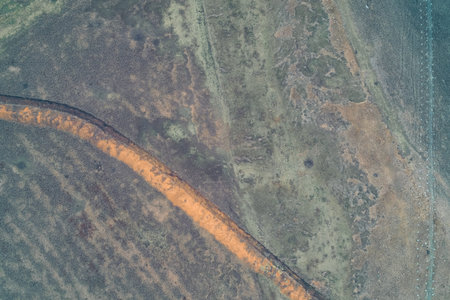Top-down aerial view of a curved anti-tank trench with orange clay embankments running parallel to...