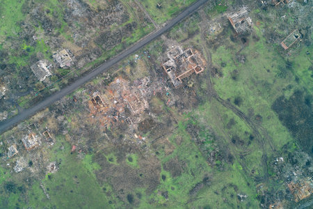 Aerial view of a village quarter reduced to ruins and foundations near vibrant green terrain surrounding it. This scene illustrates the devastating aftermath of the invasion and highlights the ongoing security risk for the European region.の写真素材
