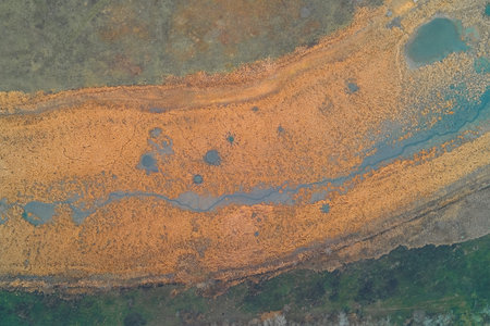 A vibrant aerial view of a marshland, dominated by a winding blue water channel that sharply...