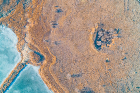 Winter field filled with dry grass next to a fragment of a frozen lake. An aerial top view showing...