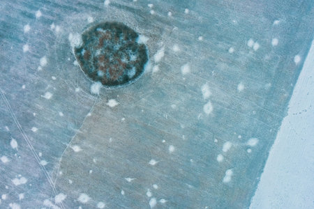 Artillery impacts and shell craters scatter across a frozen winter field near a small cluster of...
