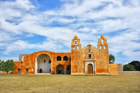 A panoramic image of the colonial convent of San Miguel Arcangel in Mani, Yucatan. Mexico, daylight, with a background of blue sky and clouds, in the foreground the green grass, color, horizontalの写真素材