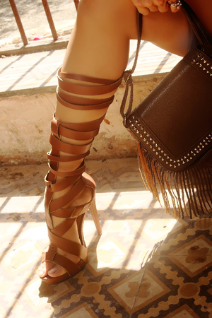 An image of a female leg, wearing a Roman sandals, and you see a leather bag in the photograph, the pose is suggestive, ambient light with flash fill, color, modeling partsの写真素材