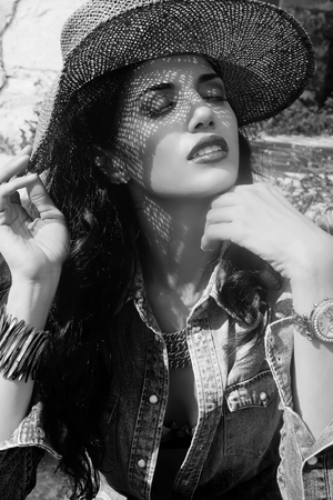 An image of an attractive young woman, make-up, covering her head with a baggy fiber hat, casting shadows over her face who has her eyes closed, is dressed in blouse and blue denim shorts, the cleavage of the blouse allows to see the brassiere Of the womaの写真素材