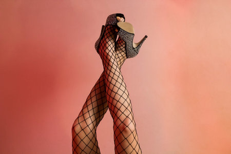Beautiful woman`s legs with black fishnet stockings and shiny heels. There is a red light reflection...