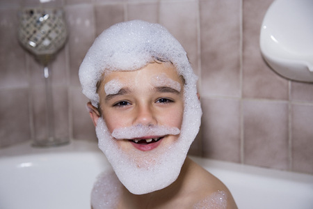 A boy bathing with foam/bubbles on he's face in the shape of a beardの写真素材
