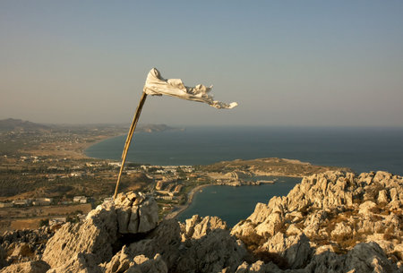 White flag on top of the mountain streaming in the wind. Panoramic view on a city near the sea.の写真素材