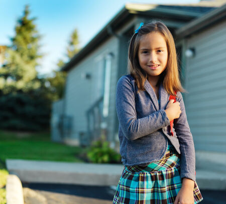 school girl with backpack standing infront of houseの写真素材