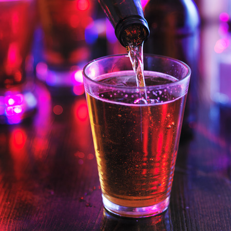 filling glass with beer from the bottle in colorful barの写真素材