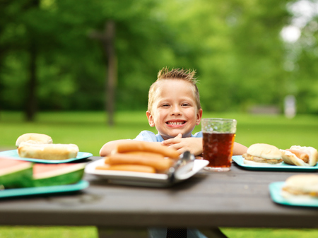 happy little boy at picnic table loaded with foodの写真素材