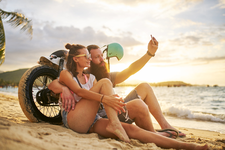 romantic tourist couple in thailand taking selfies on beach by motorbikeの写真素材