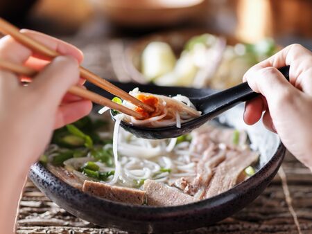 woman eating pho with sriracha using chopsticks and spoon togetherの写真素材