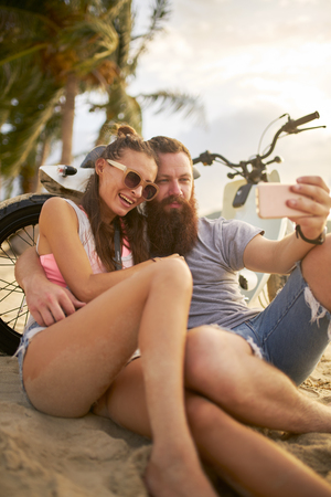 romantic tourist couple in thailand taking selfies on beach by motorbikeの写真素材