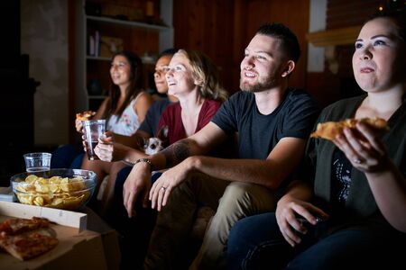 group of five friends eating pizza and drinking beer while watching tvの写真素材