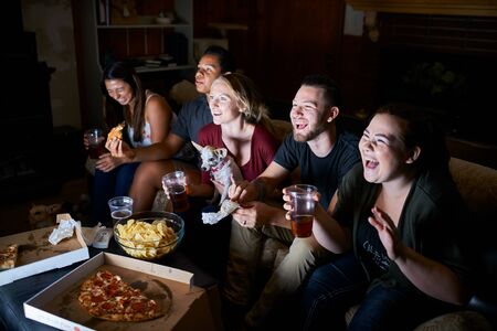 group of passionate friends cheering while watching game on tv eating pizza and drinking beerの写真素材