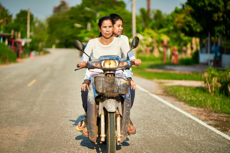 Thai mother and daughter riding motorbike together in rural thailand on roadの写真素材
