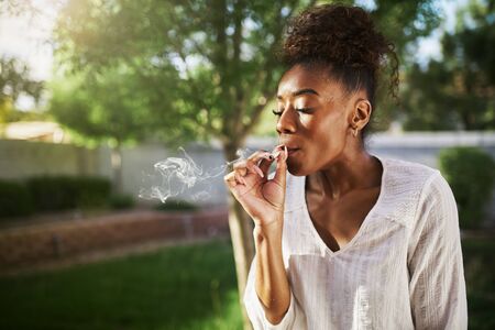 happy african american woman smoking marijuana joint in back yardの写真素材