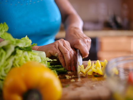 older thai woman cutting up yellow bell pepper on board to make saladの写真素材