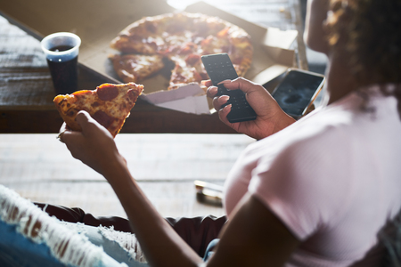 woman staying up late relaxing at home watching tv and eating pizzaの写真素材