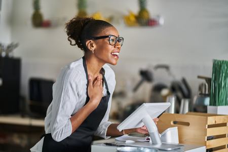 Friendly shop assistant waving and greeting customers in store while at pos terminal counterの写真素材