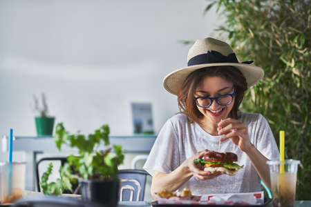 Happy smiling woman eating healthy vegan burger at trendy restaurantの写真素材