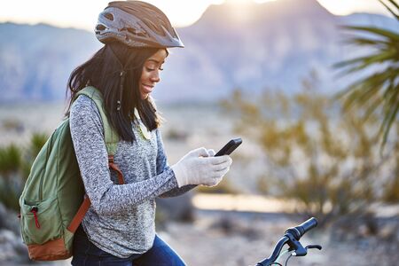 fit african american woman with bike stopping to use smartphone at red rock canyon parkの写真素材
