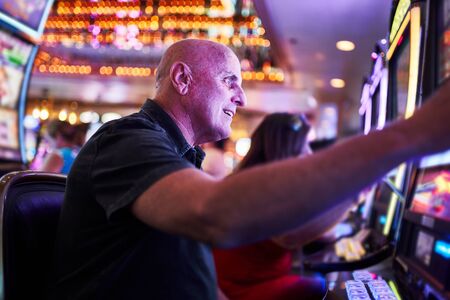 elderly tourist playing slot machines and gambling in casinoの写真素材