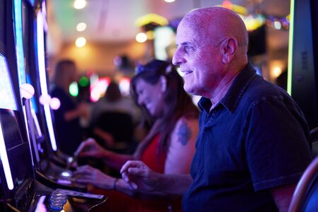 elderly tourist playing slot machines and gambling in casinoの写真素材