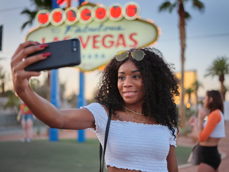 african american woman taking selfie with smartphone in front of welcome to las vegas sign