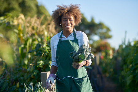 African american woman holding freshly picked kale from communal community garden posing for...