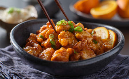 eating bowl of chinese orange chicken with chopsticksの写真素材