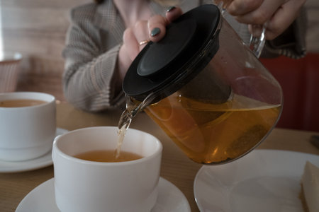married woman pouring a cup of tea in a cafe in a white mugの写真素材