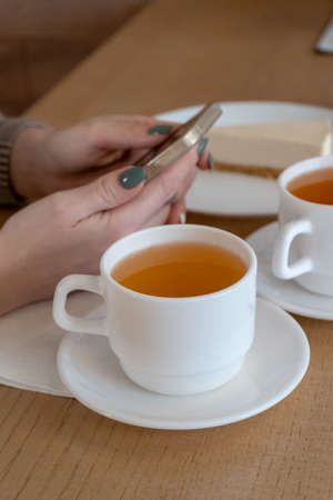 two cups of tea and a cheesecake cake a girls hand with a phone in her hands in a cafe daylight lunch lunch snackの写真素材