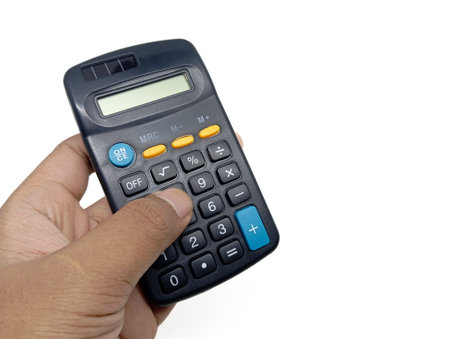 A hand is holding and pressing buttons on a dark-colored calculator with yellow and blue accents, isolated against a bright white background, conveying action in calculation or accounting.の写真素材