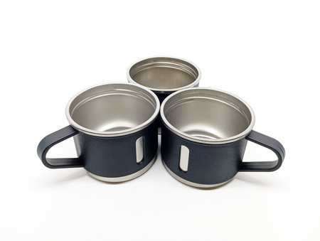 Top view of three empty stainless steel mugs with black handles arranged in a triangle on a white background, ideal for kitchenware or outdoor equipment visuals.の写真素材