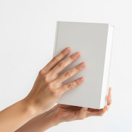 Hands holding a closed white book against a white backgroundの素材