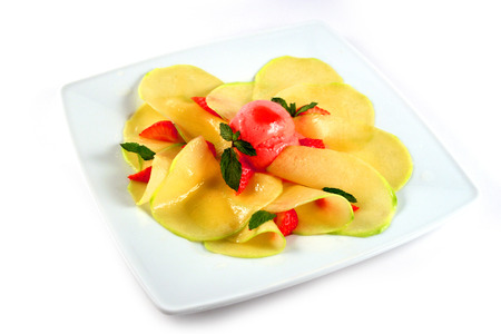 Mango carpaccio with ice-cream, strawberry and mint on white plateの写真素材